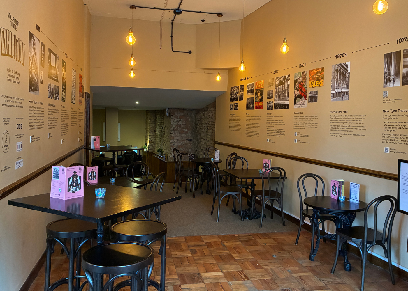 Stoll exhibition – 1867 Cafe Bar A photograph of the new Stoll Exhibition displayed on the walls of the 1867 Café at Tyne Theatre and Opera House. The exhibition spans the walls on either side of the cafe, displaying archival images and text, with QR codes for interactive elements.